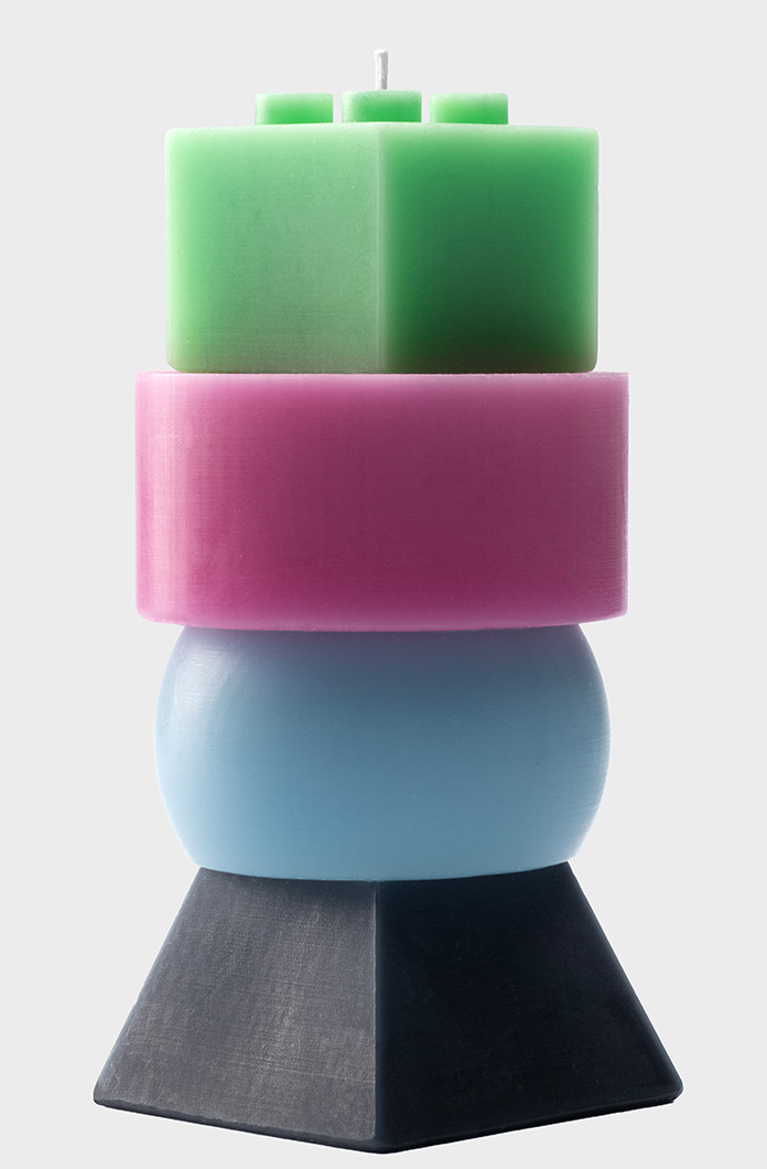 Colorful stacked geometric candle with green square top pink circular center blue spherical layer and black pyramid base on a neutral background modern decor item