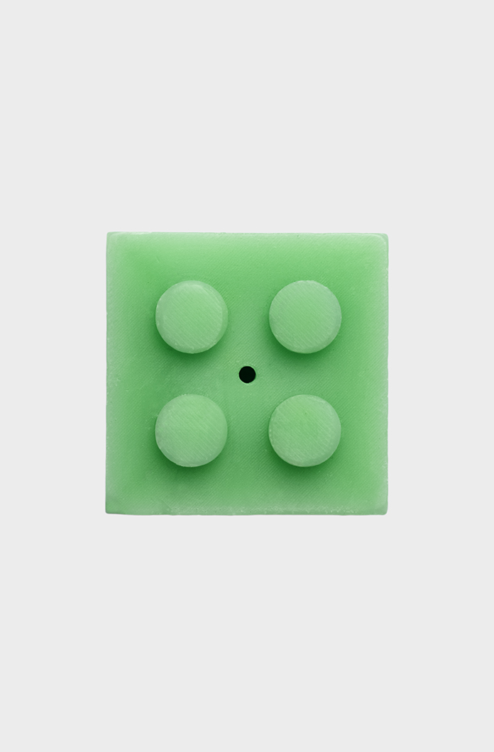 Green square LEGO-style candle with four round studs on a light gray background. Perfect for unique bathroom decor and quirky gift ideas. Ideal for LEGO enthusiasts.